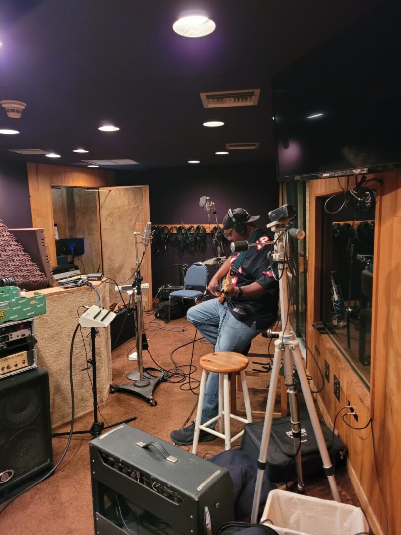 A person playing the guitar inside a studio or room.